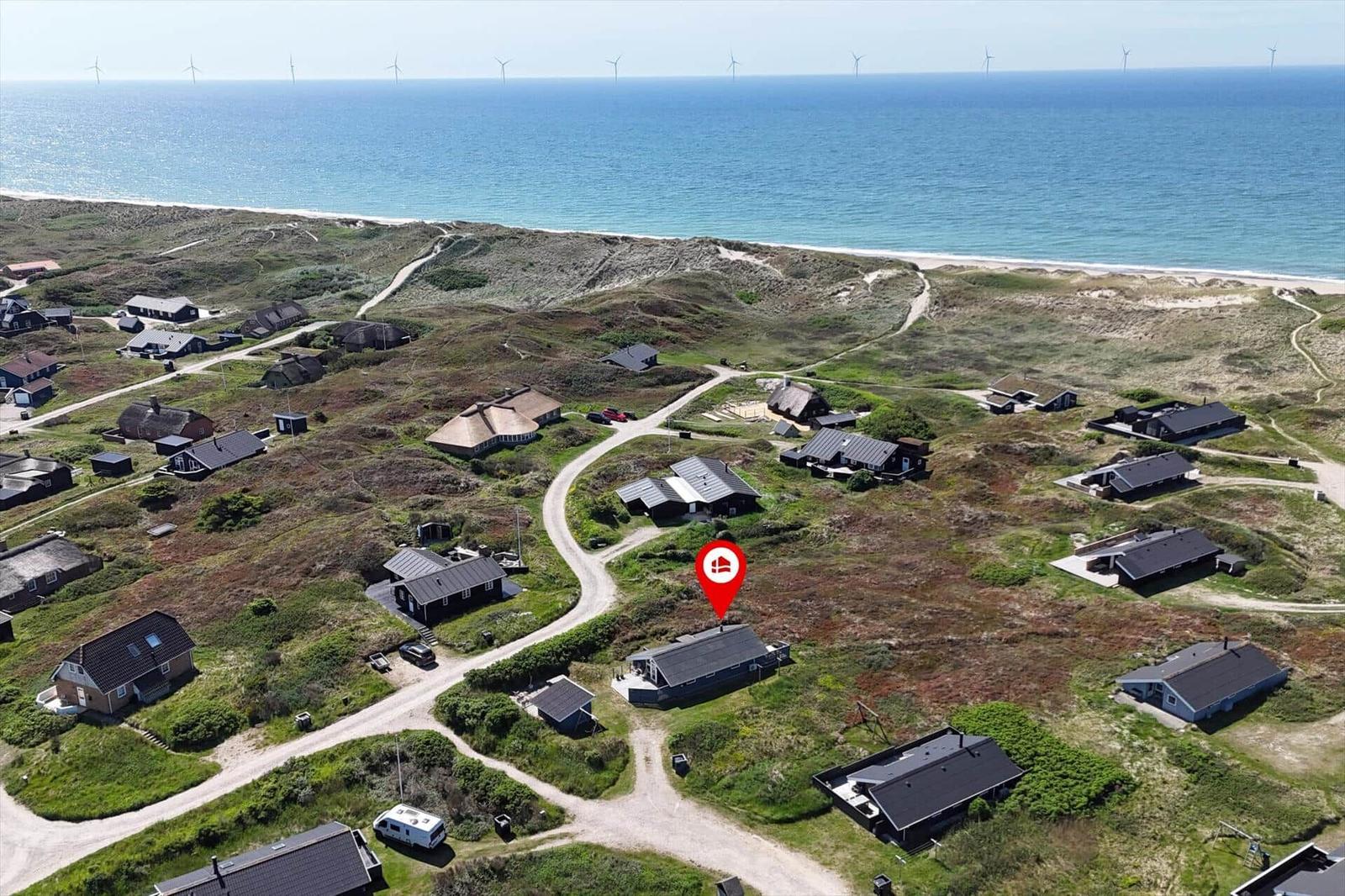 Hütten am Strand mit Blick auf das Meer und Windräder im Hintergrund.