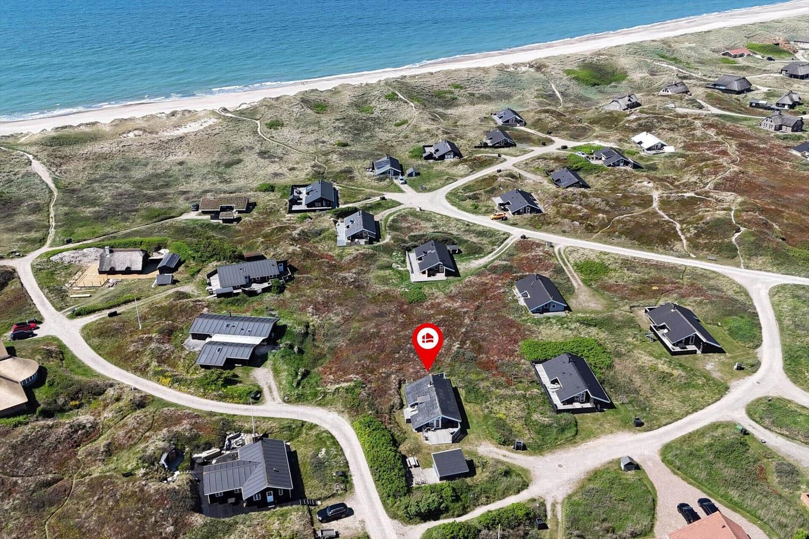 Aerial view of vacation homes near beach with paths and dunes.