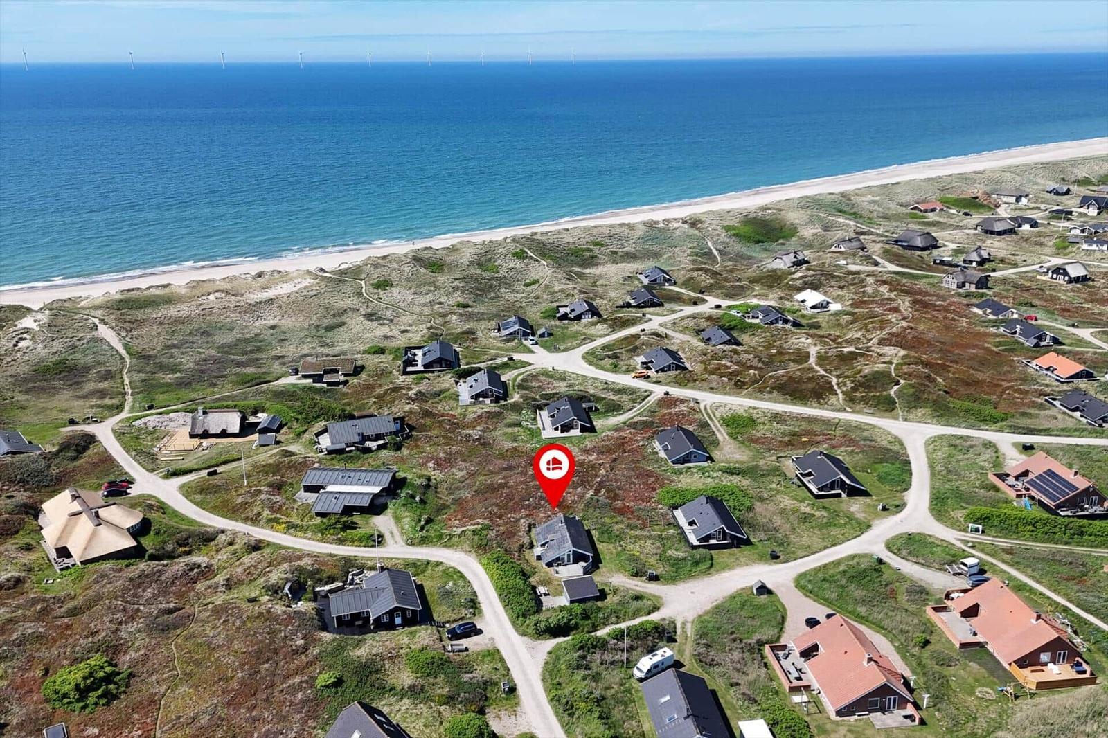 Aerial view of coastal vacation homes with beach and wind turbines in distance.