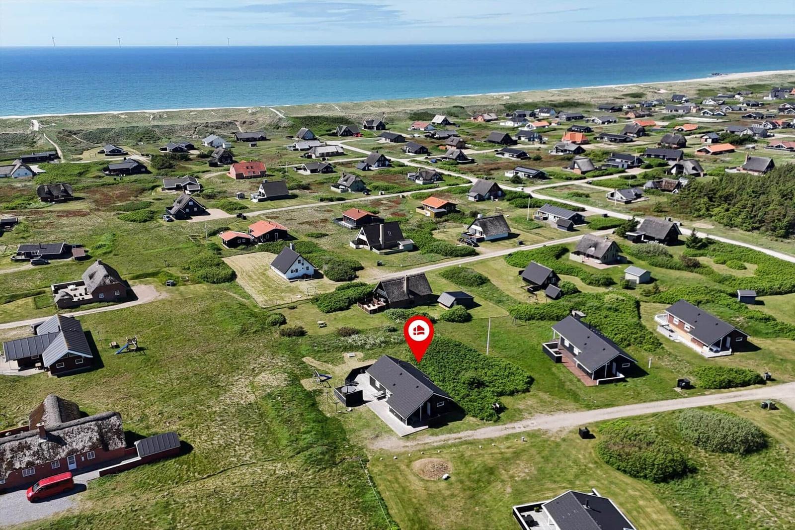 Haus mit rotem Markierungspunkt in grüner Landschaft nahe Strand und Meer.