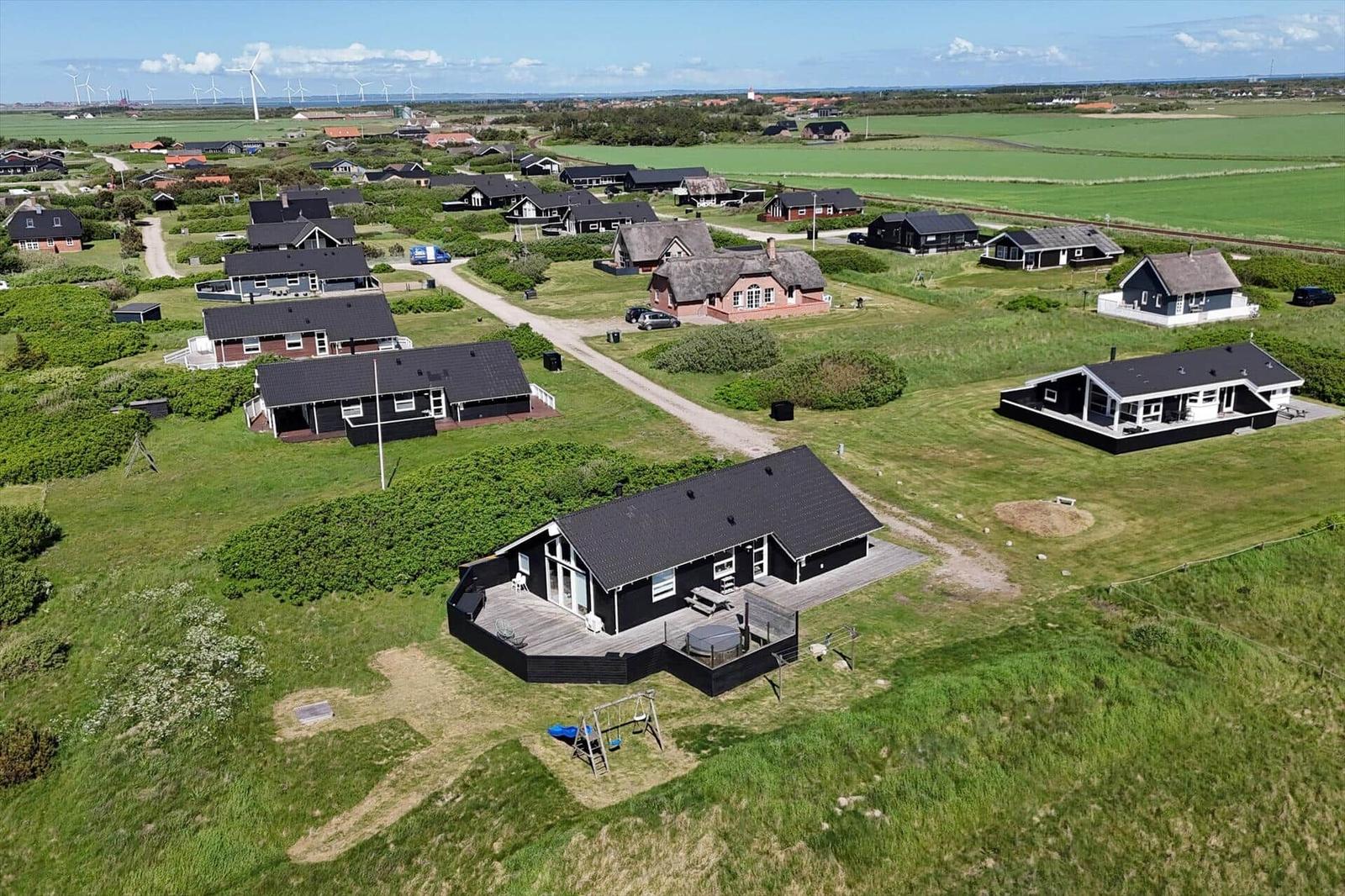 Aerial view of holiday homes with grassy terrain and wind turbines in the distance.