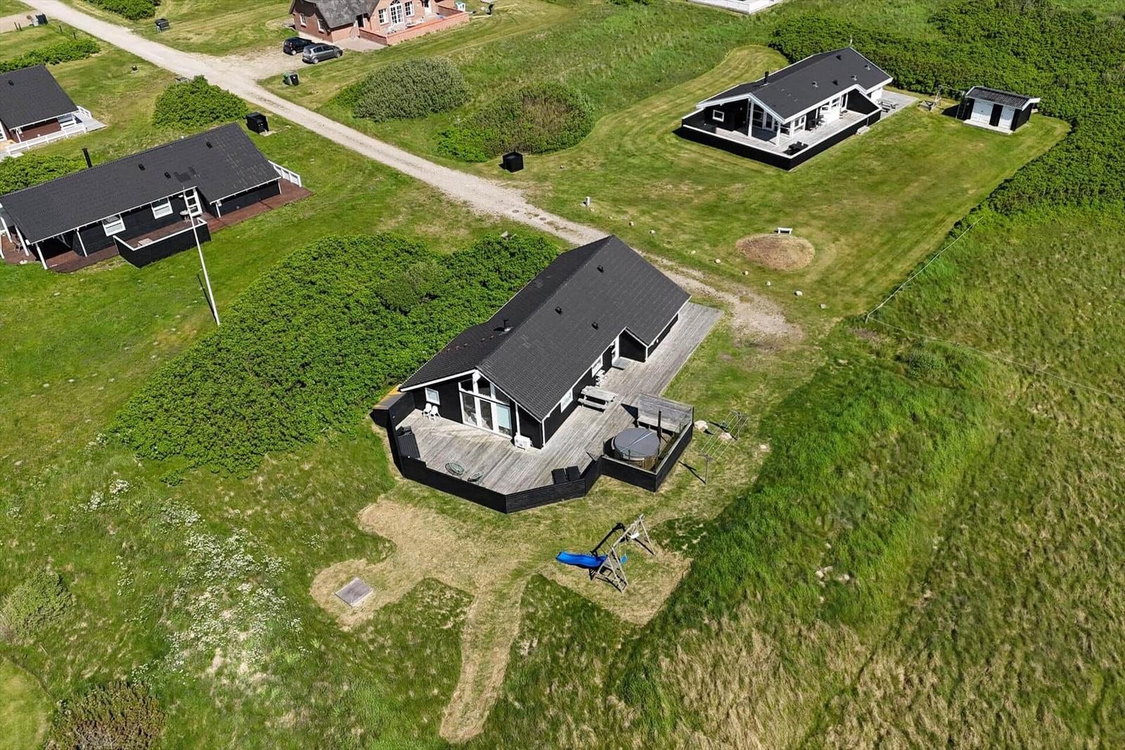 Haus mit Holzterrasse, Whirlpool und Spielplatz auf grünem Grundstück.