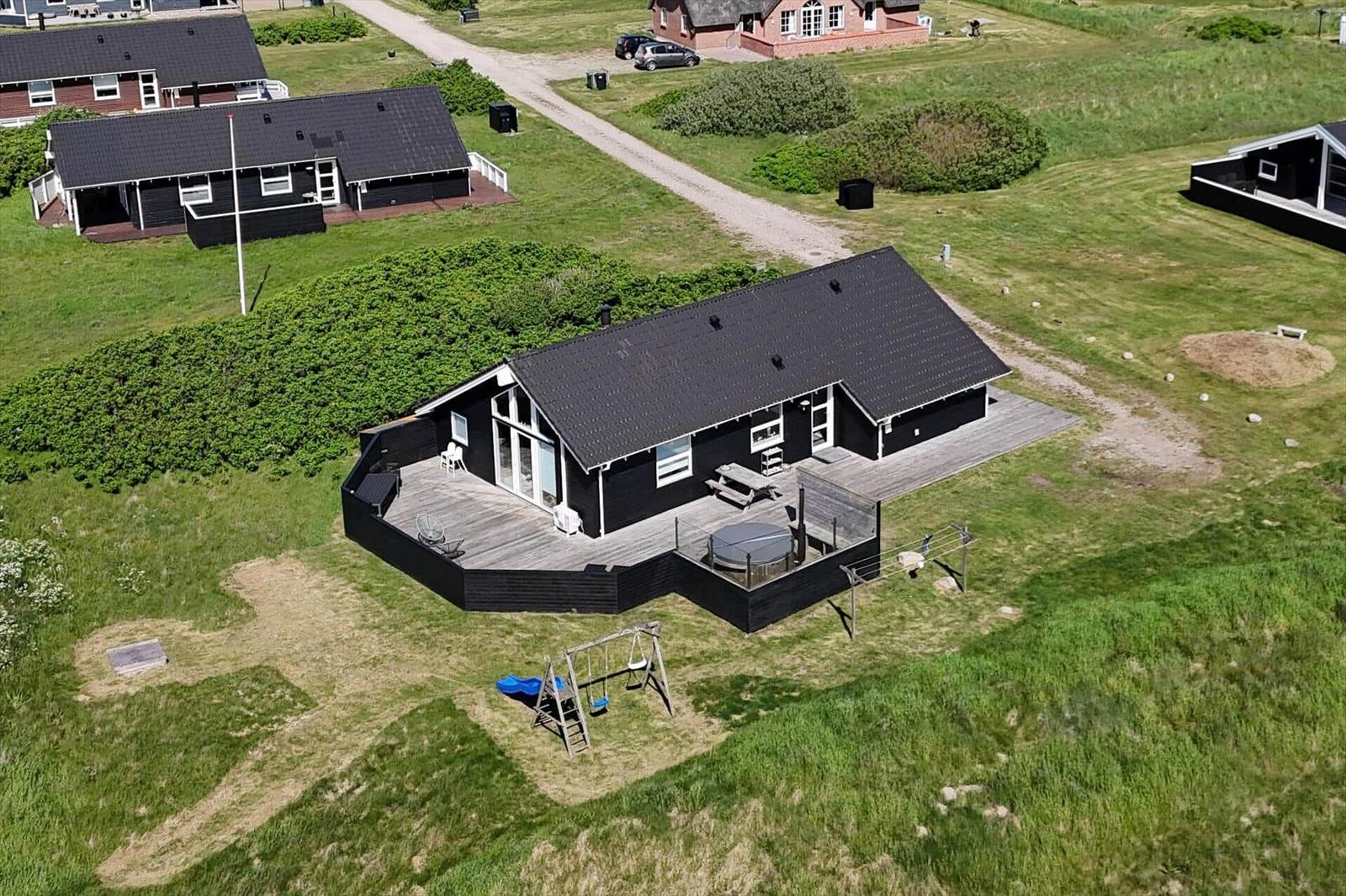 Schwarzes Haus mit Terrasse, Grillplatz und Spielplatz auf grünem Grundstück.