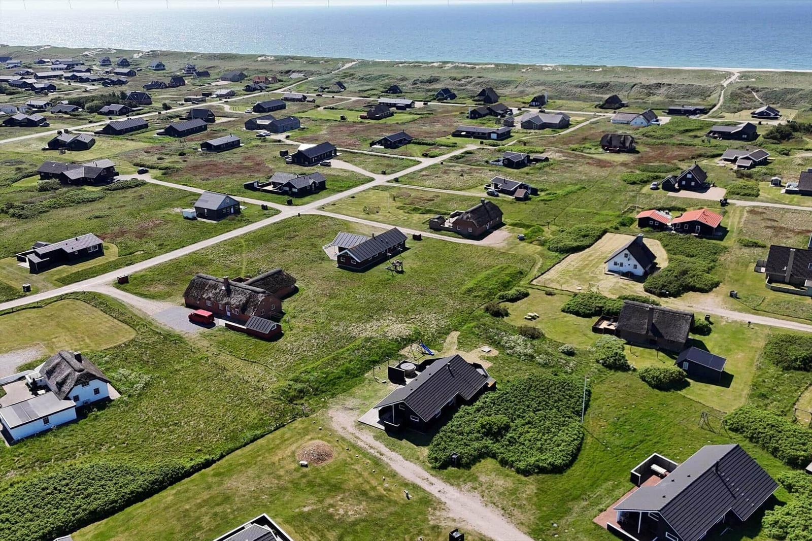 Aeriale Aufnahme von Ferienhäusern an der Küste mit Grünflächen und Strand.