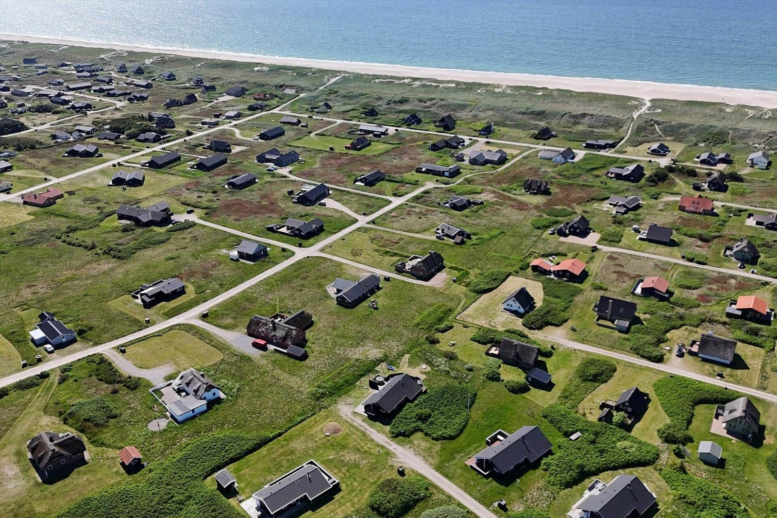 Aerial view of a coastal village with houses, greenery, and a sandy beach.