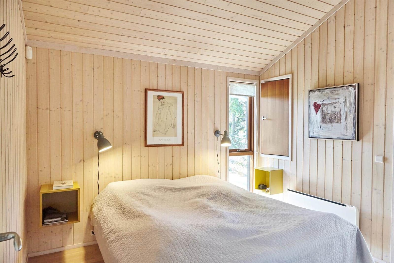 Zimmer mit Holzwand, zwei Betten, Wandlampe und Bild an der Wand.