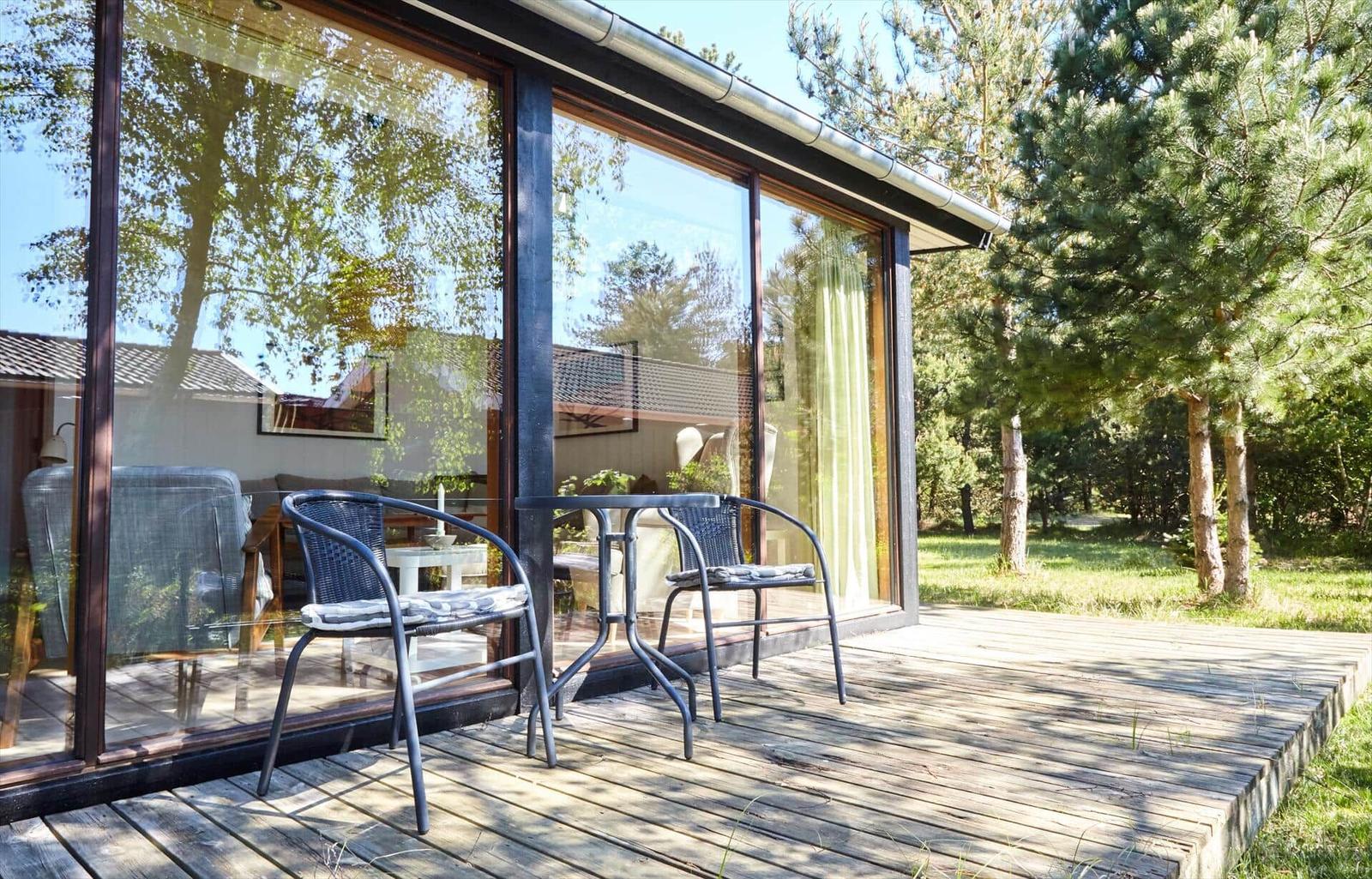 Terrasse mit Tisch und Stühlen vor einem Haus mit Glasfassade und Blick auf Bäume.