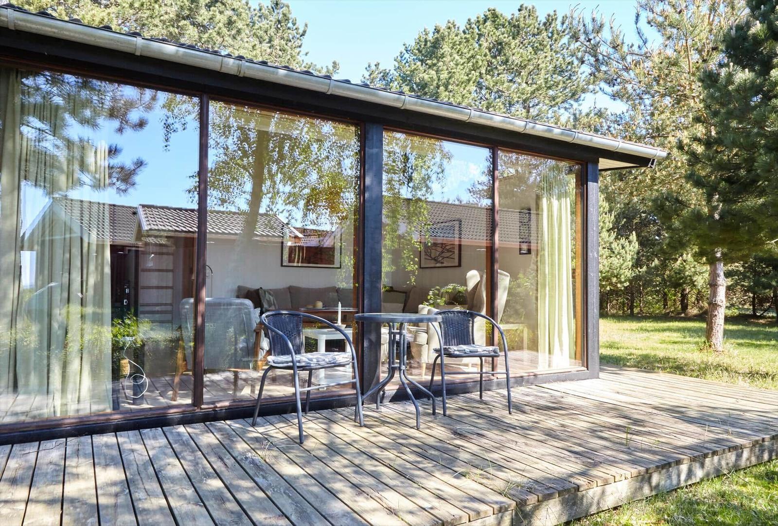 Haus mit Terrasse, Sitzbank und Sonnenschirm unter Bäumen.