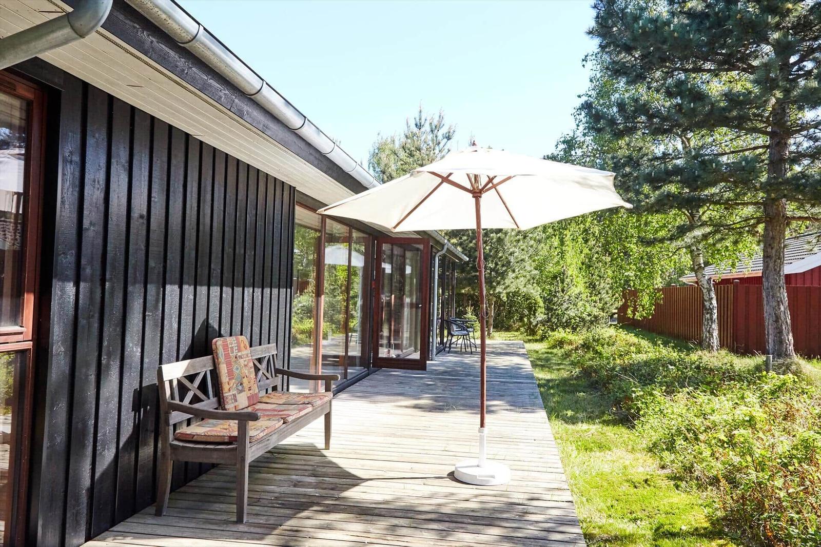 Schwarzes Holzhaus mit Dach und Terrasse umgeben von Bäumen und Gras.