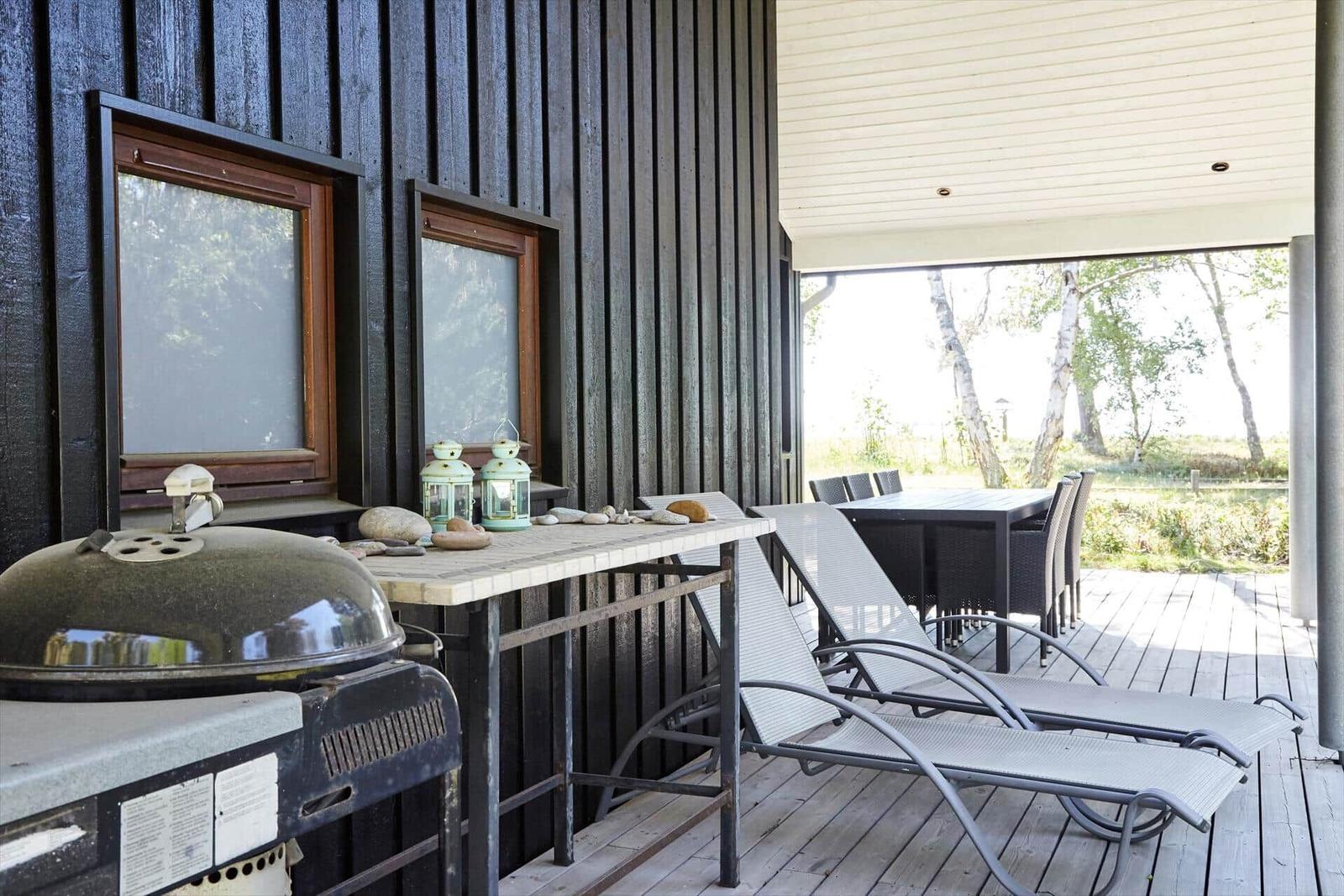 Ein dunkelholzverkleidetes Ferienhaus mit Terrasse, Garten und Bäumen im Hintergrund.