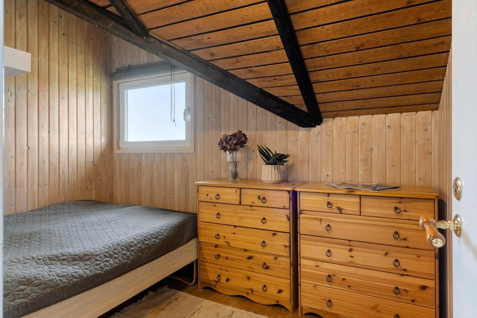 Schlafzimmer mit Holzwand, Bett und Doppelbett. Holzdecke mit Trägern.