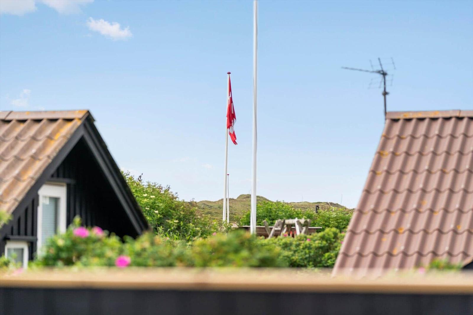 Schwarzes Ferienhaus mit Terrasse und Garten. Umgeben von weiteren Häusern und Grünflächen.
