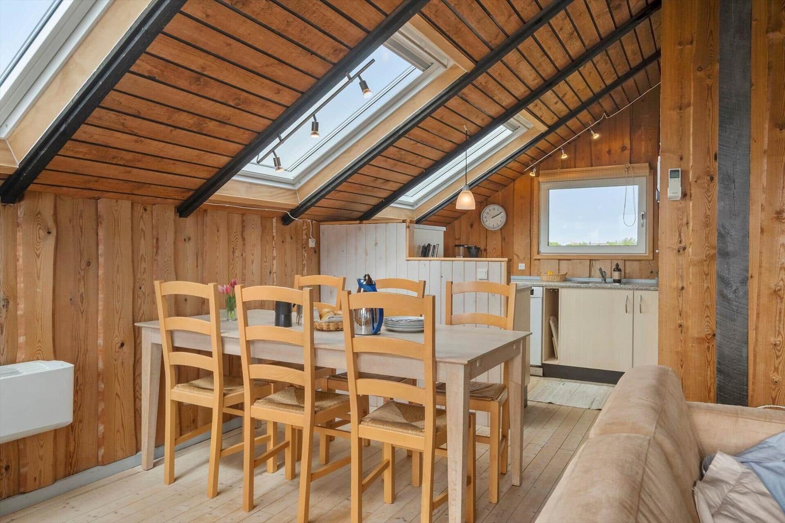Esstisch mit Stühlen, Kaffeekanne und Brot im Holzhaus mit Dachfenster.
