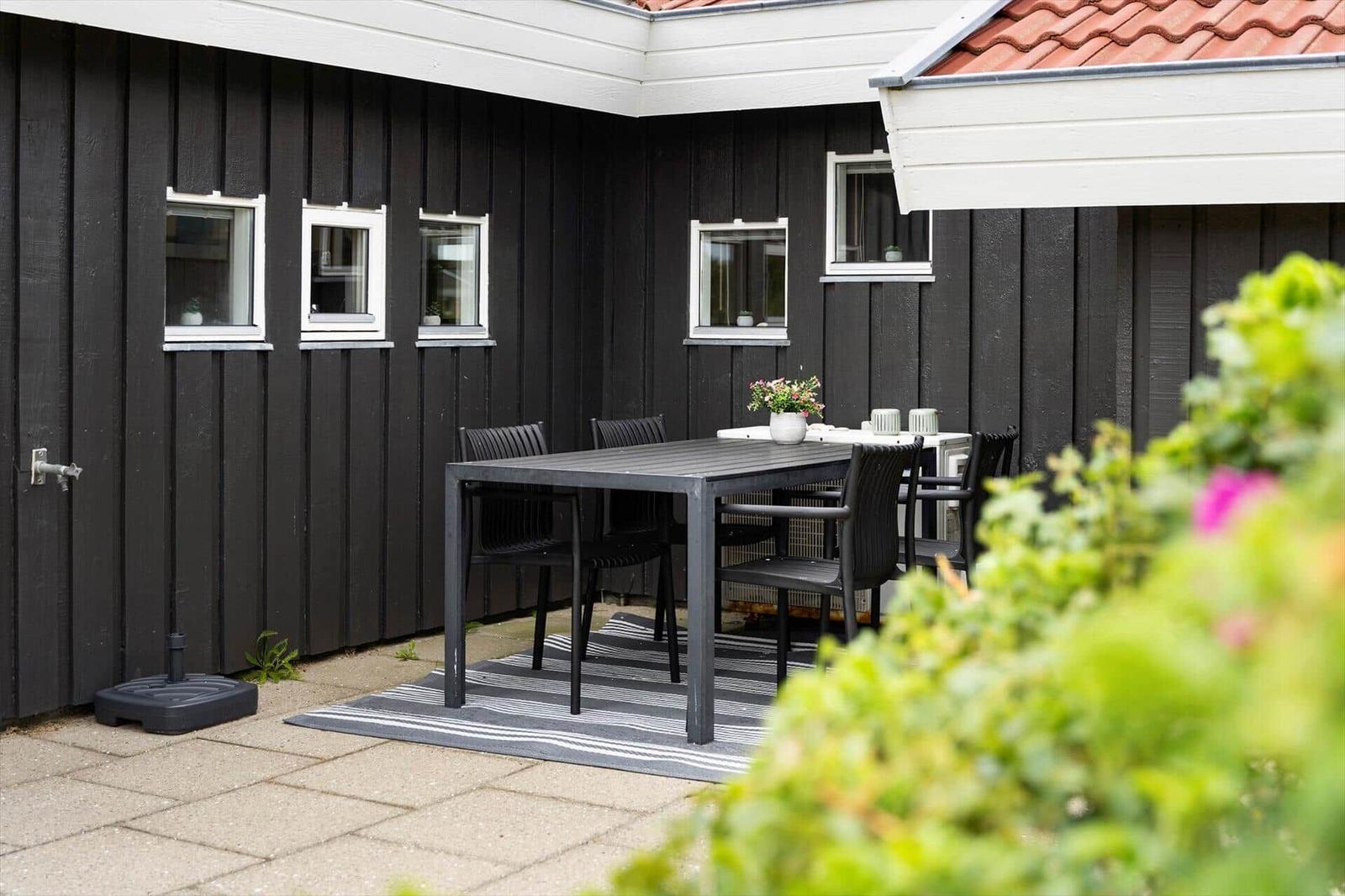 Terrasse mit Picknicktisch, dunkler Holzwand und Pflanzen im Vordergrund.