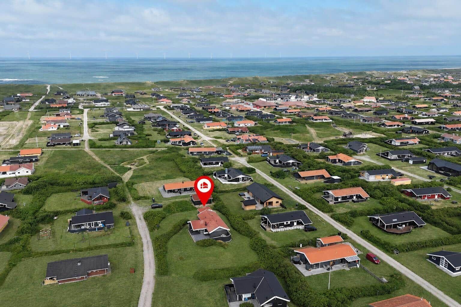 Aerial view of a coastal village with houses and wind turbines in the distance.