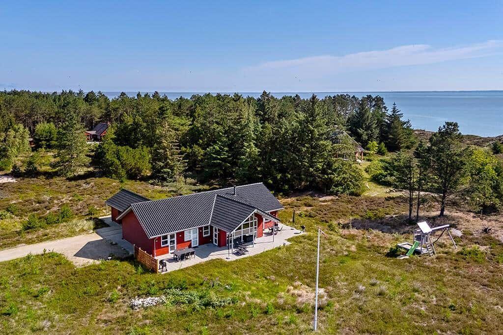 Rotes Ferienhaus mit großem Glasbereich und Terrasse im Grasland.
