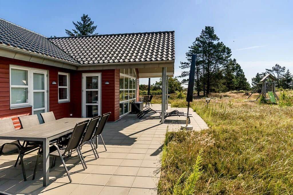 Roter Holzhaus mit Whirlpool im Garten. Umgeben von Gräsern und Bäumen.