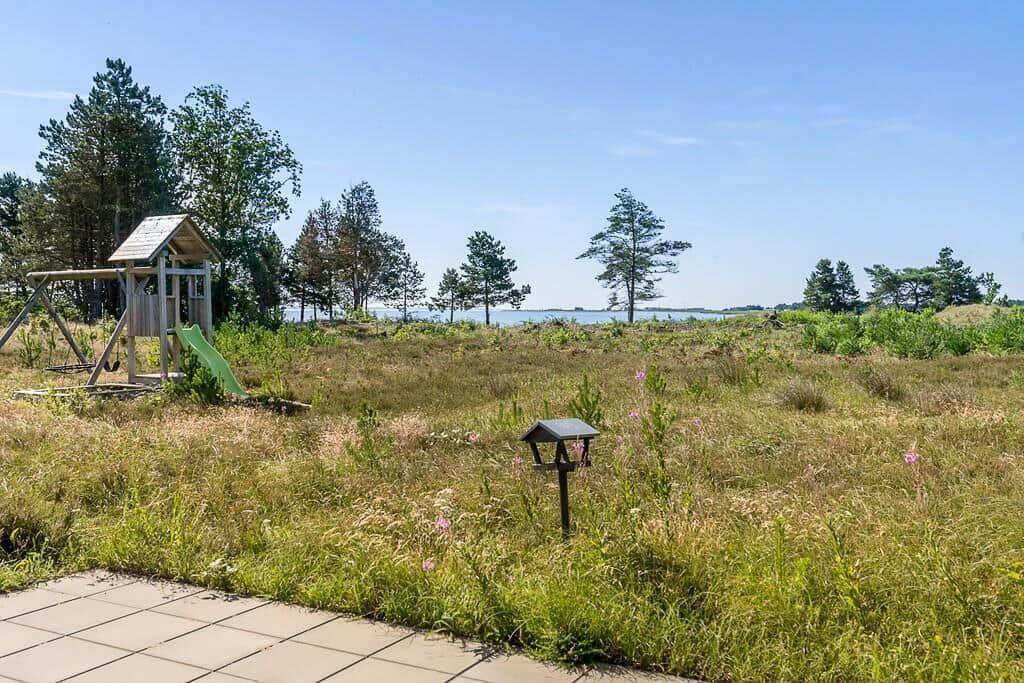 Terrasse mit Tisch, sechs Stühlen und Grill. Hintergrund: Holzzaun und Wohnhäuser.