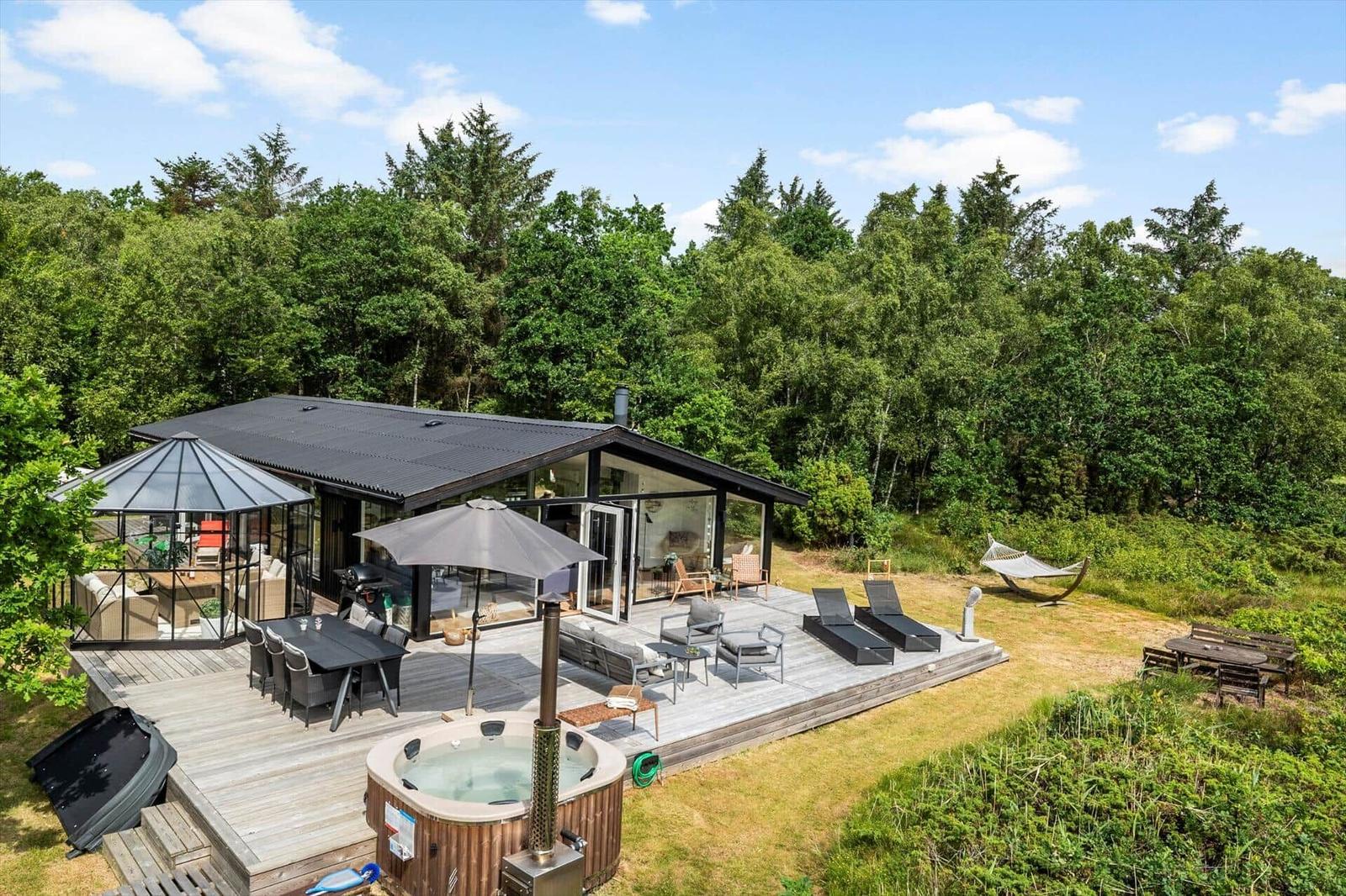 Moderne Villa mit großem Terrassenbereich, Whirlpool und Hängematten in grüner Umgebung.