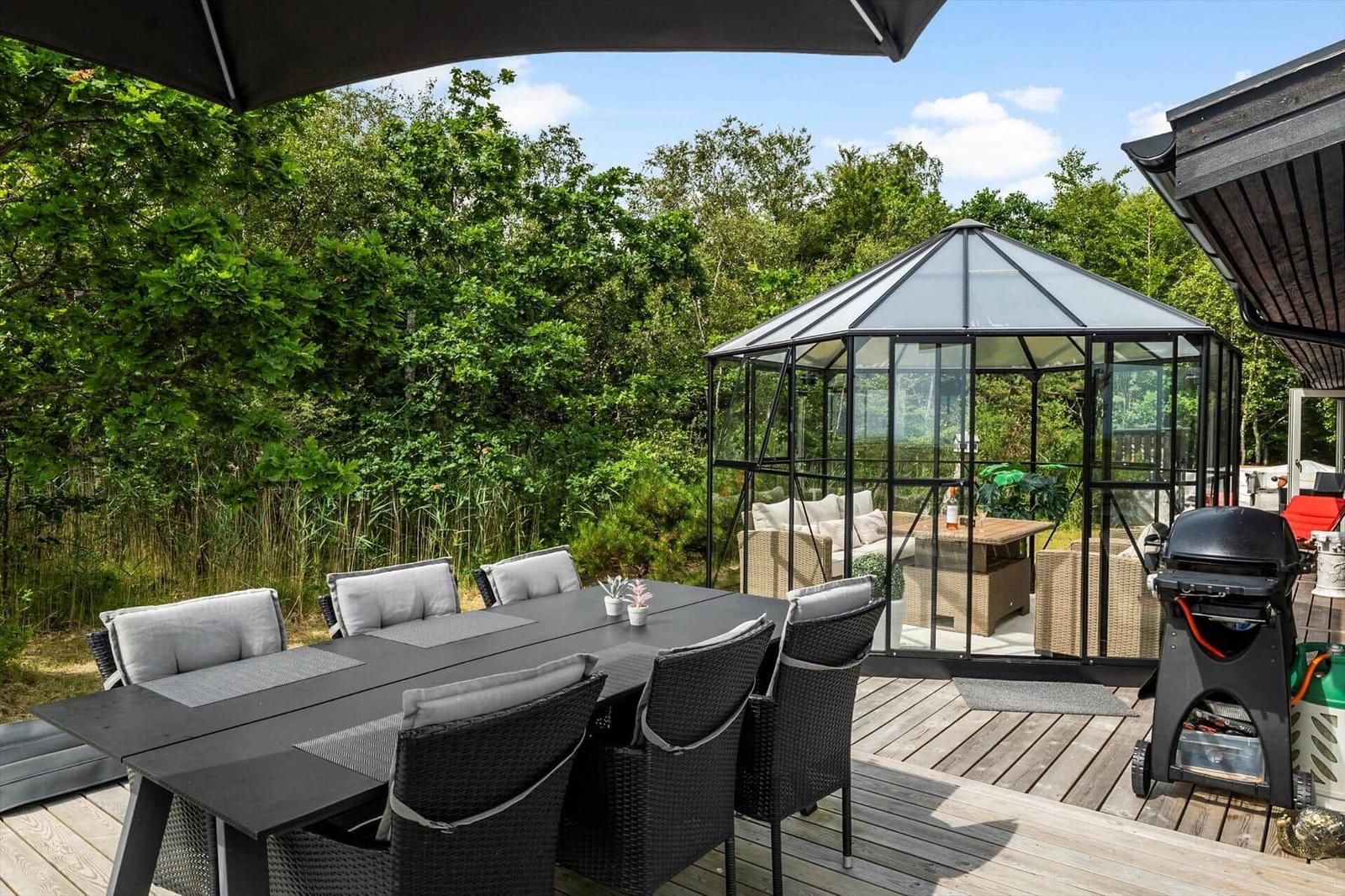 Terrasse mit Tisch, zwei Gläsern und einer Flasche Wein. Hintergrund: Glaswand und grüne Pflanzen.