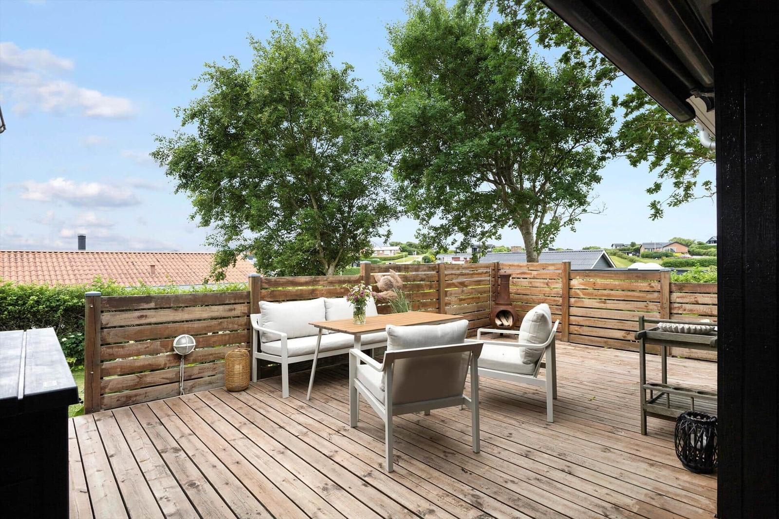 Terrasse mit Sitzgruppe, Tisch und Pflanzen. Holzdecke und Zaun. Blick auf Landschaft.