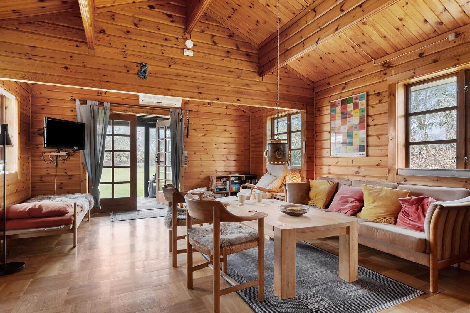 A bed with pillow and lamp next to a window with view of green. A book lies on wood.