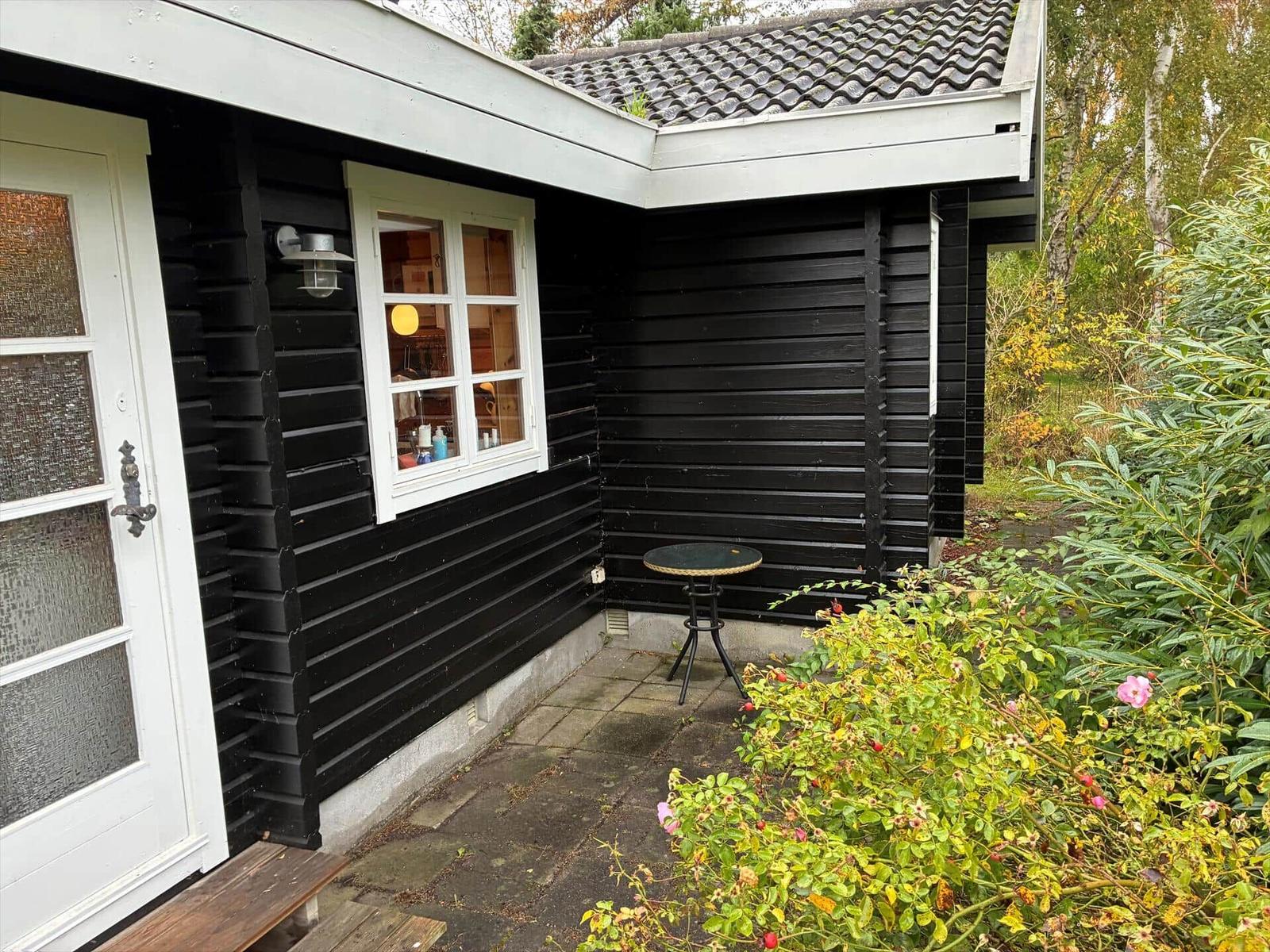A black wood stove with a burning fire is against a stone wall and wooden ceiling.