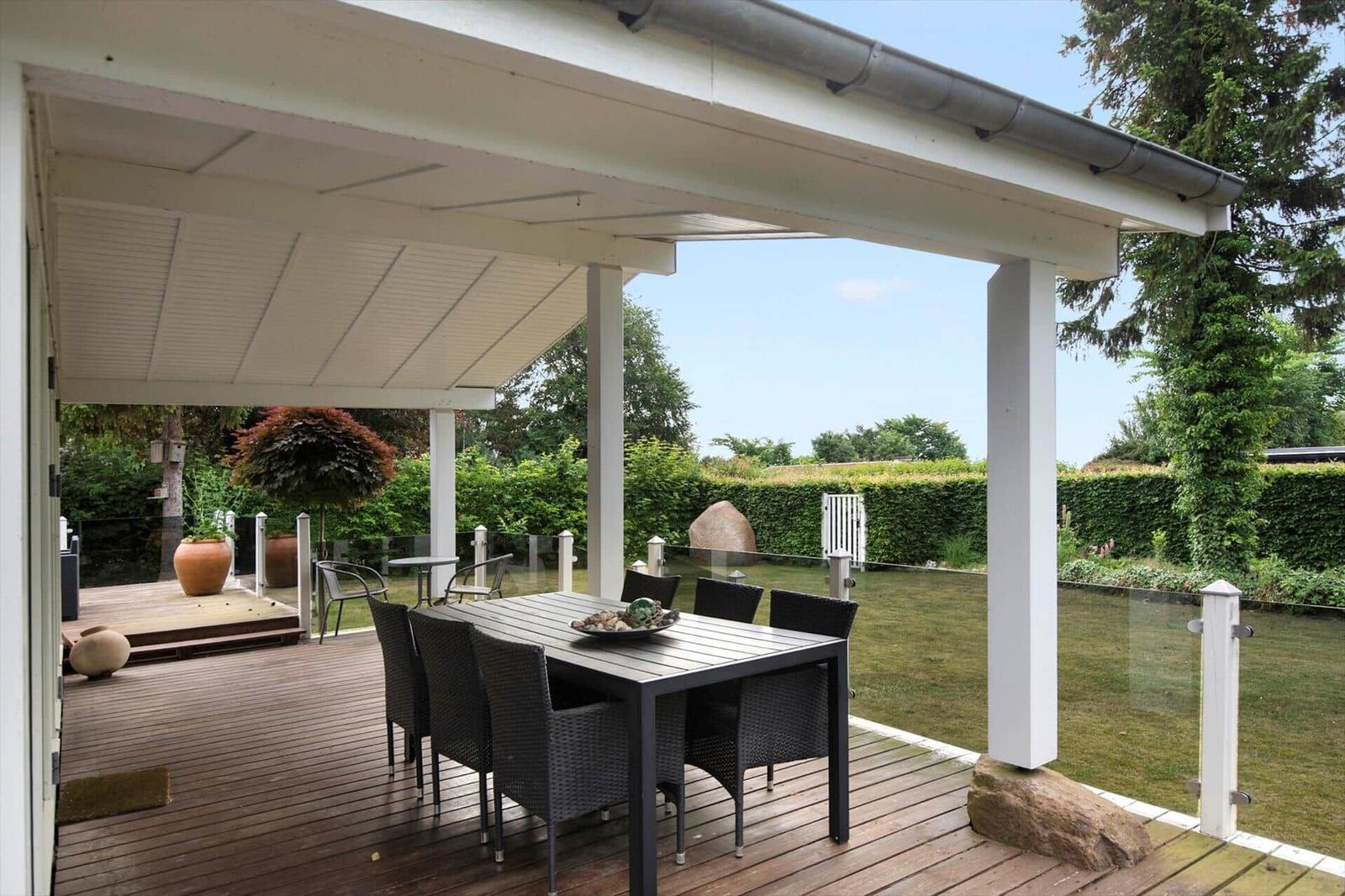 Moderne Villa mit großem Balkon und Garten. Terrasse mit Sitzgelegenheiten und Blick auf Bäume.