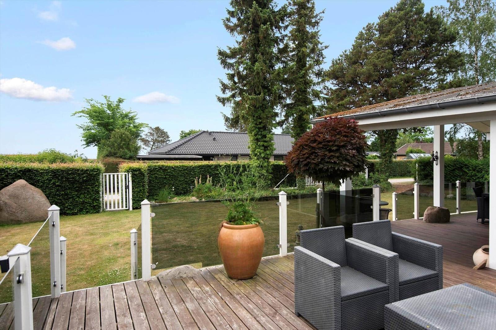 Hinterhof mit Tisch, Stühlen und Holzbadewanne. Weiße Hauswand und Glasfront.