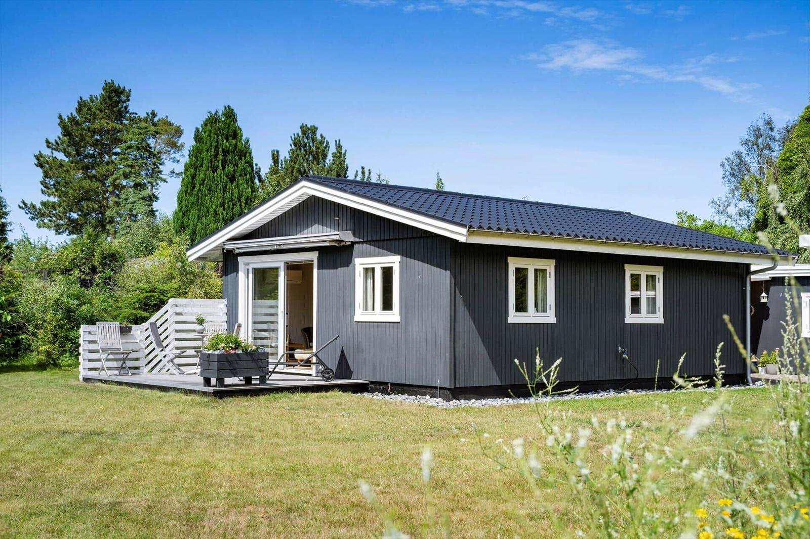 A gray wooden house with white trim and a terrace in the garden.
