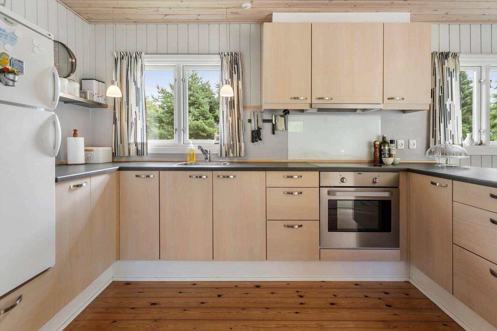 Kitchen with wooden cabinets, stainless steel oven, and windows to the garden.