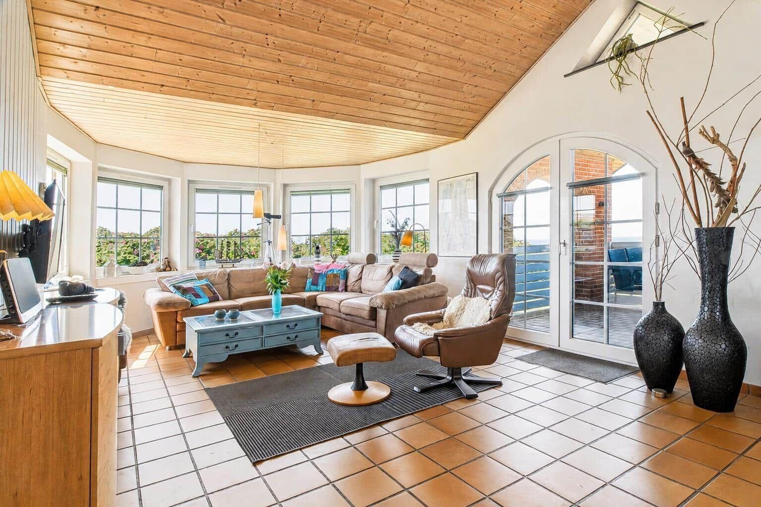 Wohnzimmer mit Holzdecke, Sofa, Sessel und Fenstern mit Blick.