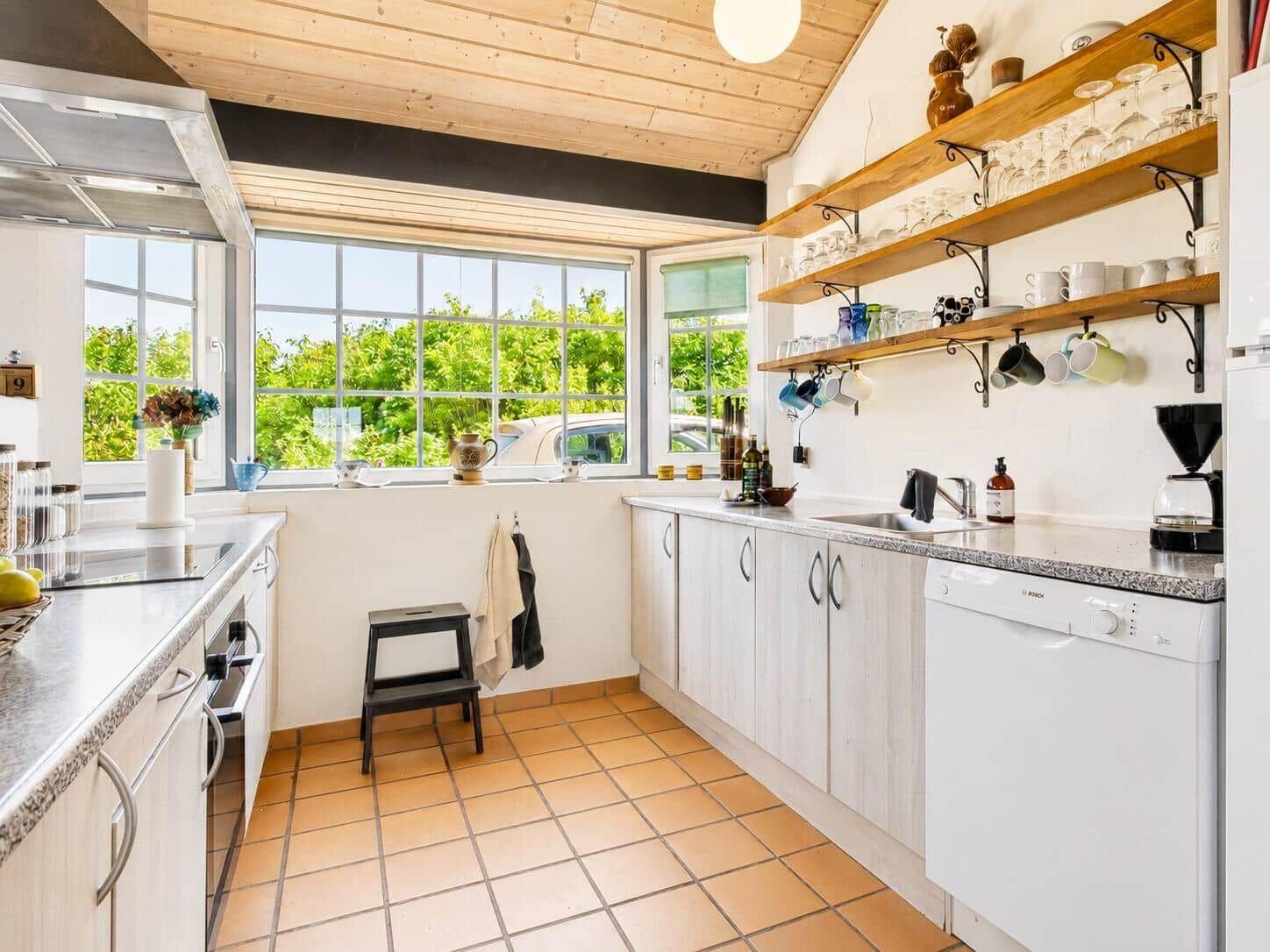 Küche mit Holzdecke, Fenstern zum Garten und Küchenzeile mit Spüle und Waschmaschine.