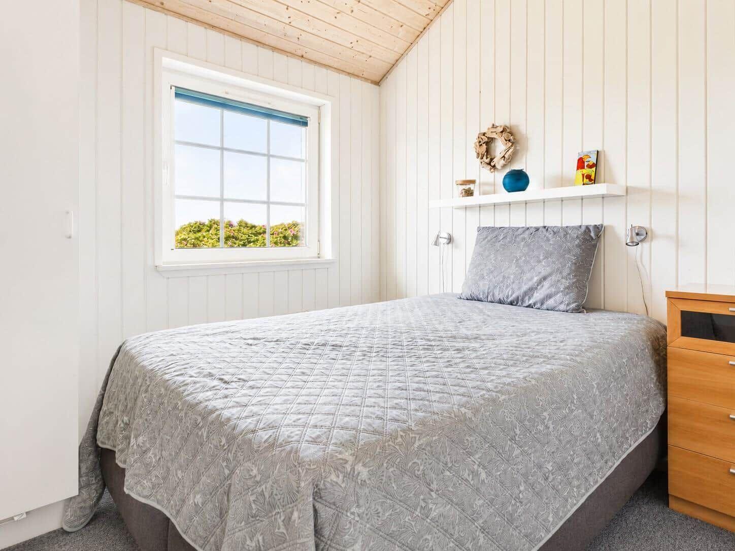 Schlafzimmer mit Bett, Fenster und Nachttisch. Wandverkleidung und Holzdecke.