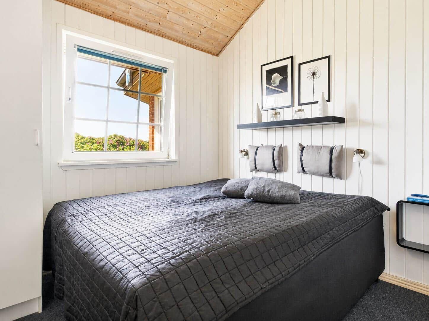 Schlafzimmer mit Bett, Fenster und Wandregal mit Dekoration.