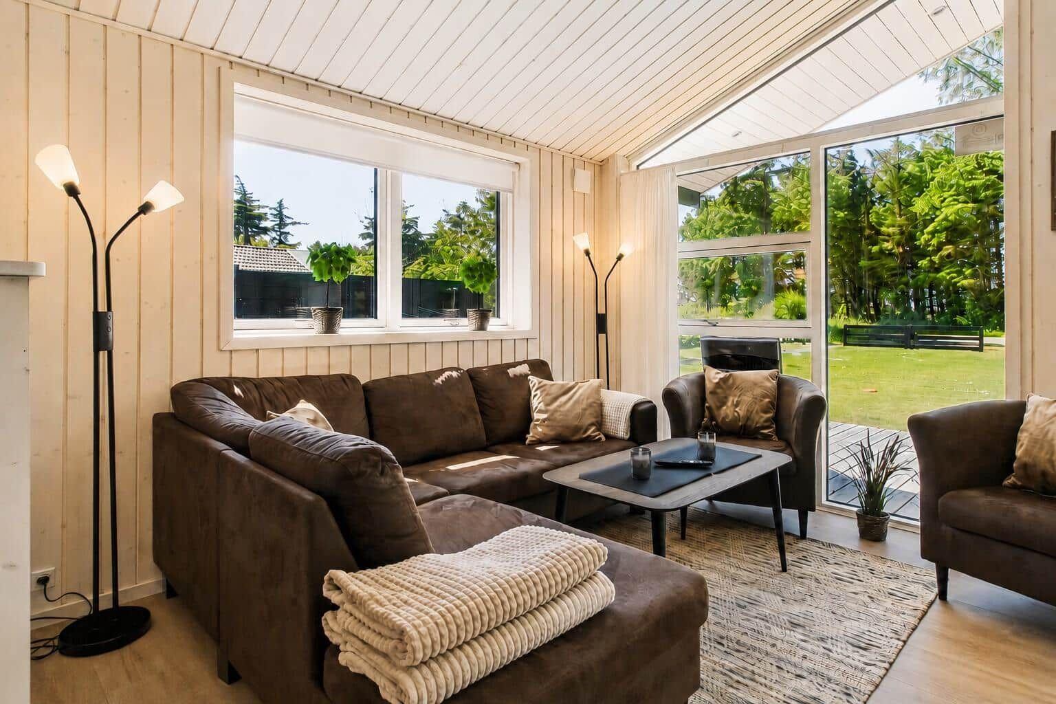 Wohnzimmer mit braunen Sofas, Tisch und Blick auf grünen Garten.