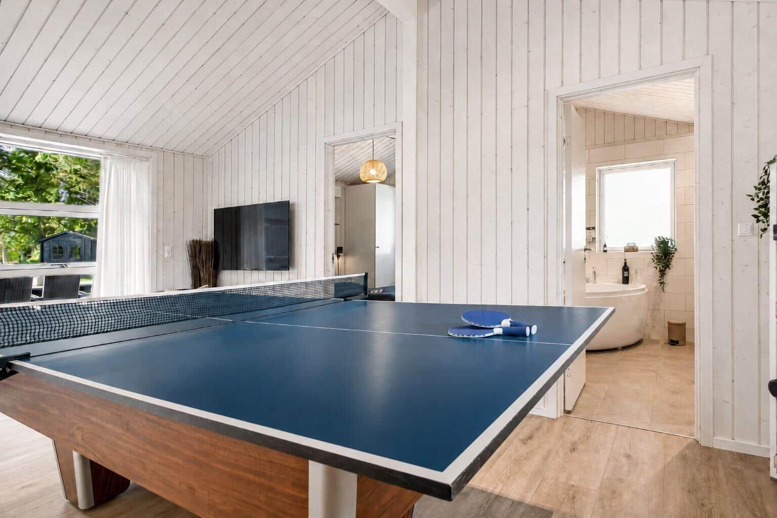 Tischtennisplatte mit Tischtennisschlägern. Im Hintergrund Bad mit freistehender Badewanne.