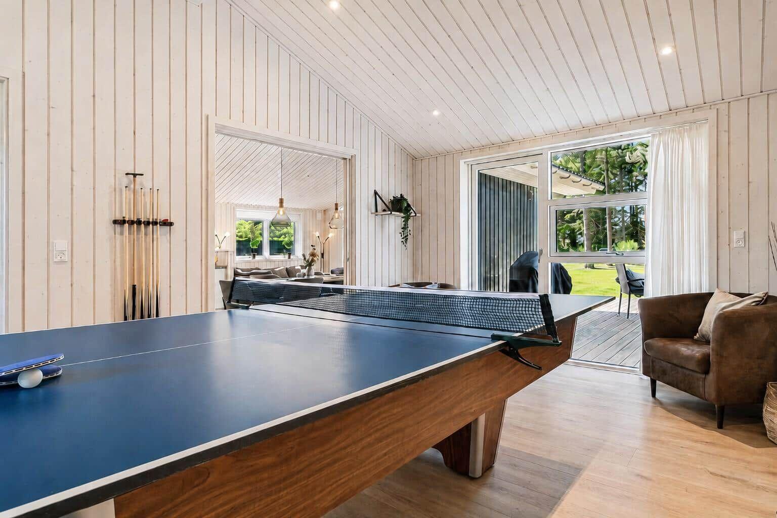 Tischtennisplatte mit Tischtennisschlägern und Ball. Durchgang zu Wohnzimmer und Terrasse.