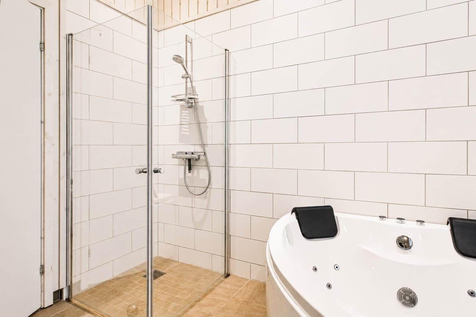 Dusche mit Glaswand und Whirlpoolbad mit schwarzen Auflagen.