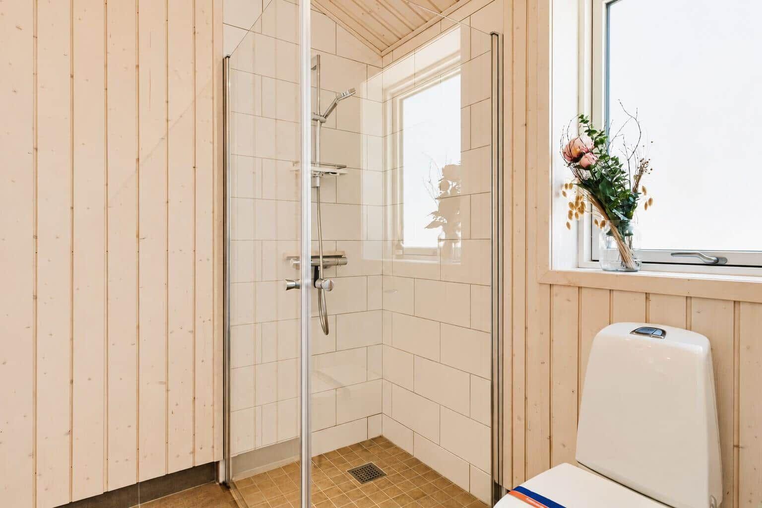 Duschkabine mit Glaswand, Toilette und Fenster mit Blumenvase.