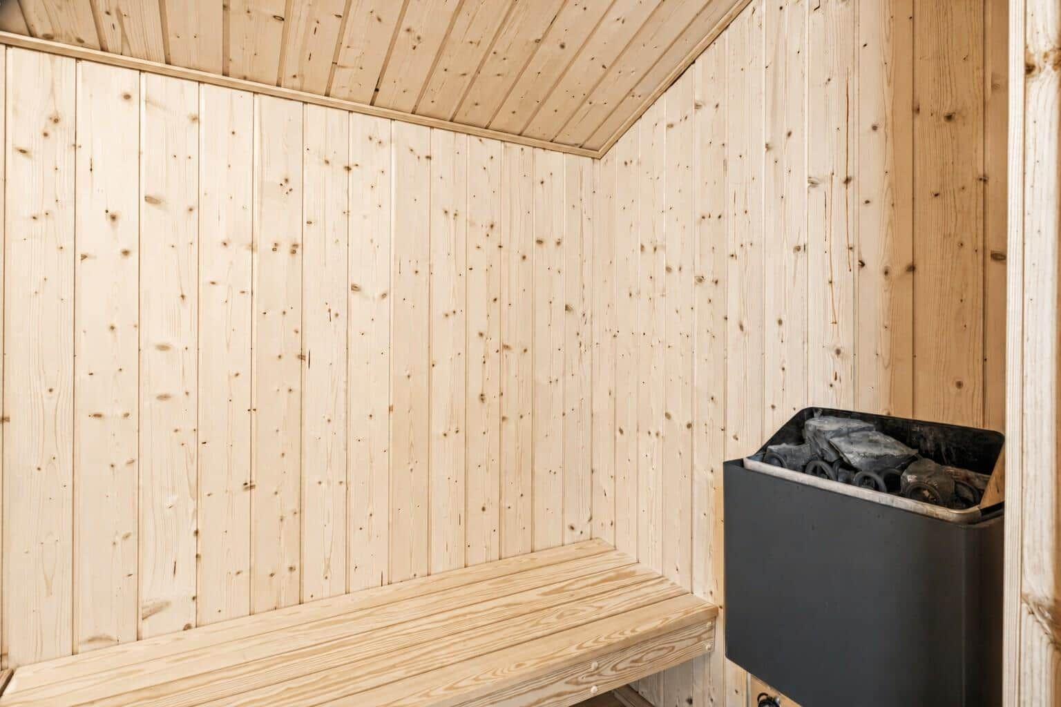 Sauna mit Holzwand und Sitzbank sowie Heizung mit Brennholz.