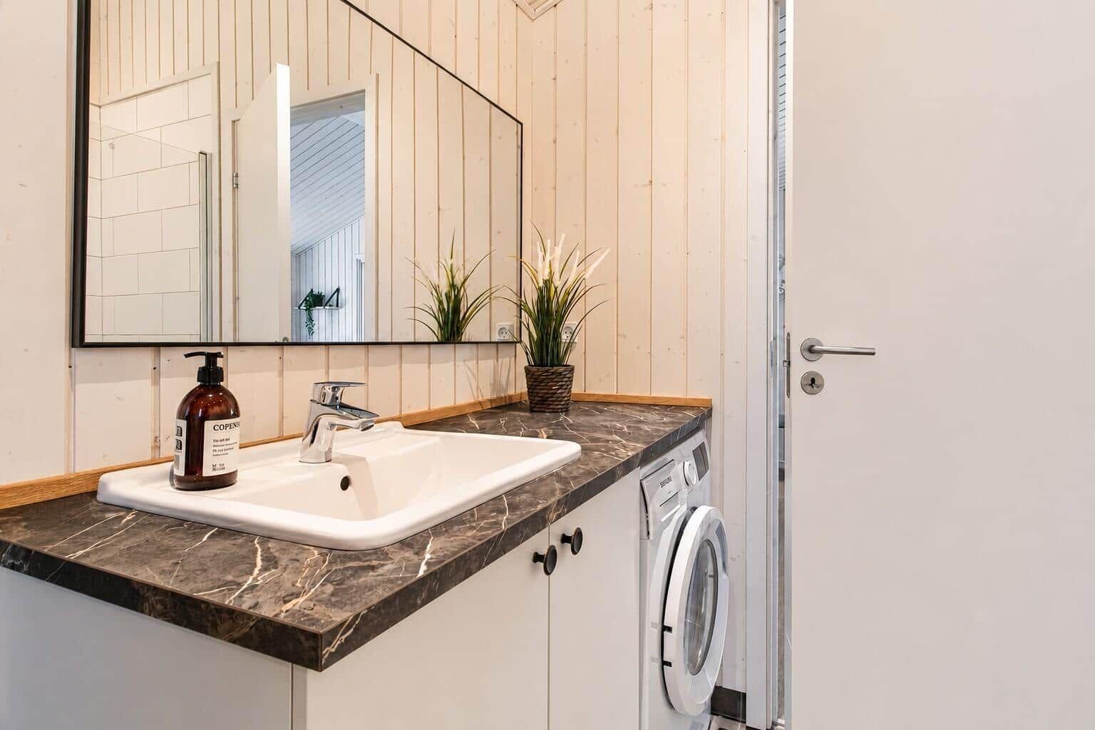 Waschbecken mit Spiegel und Waschmaschine in einem Badezimmer mit Holzwandverkleidung.