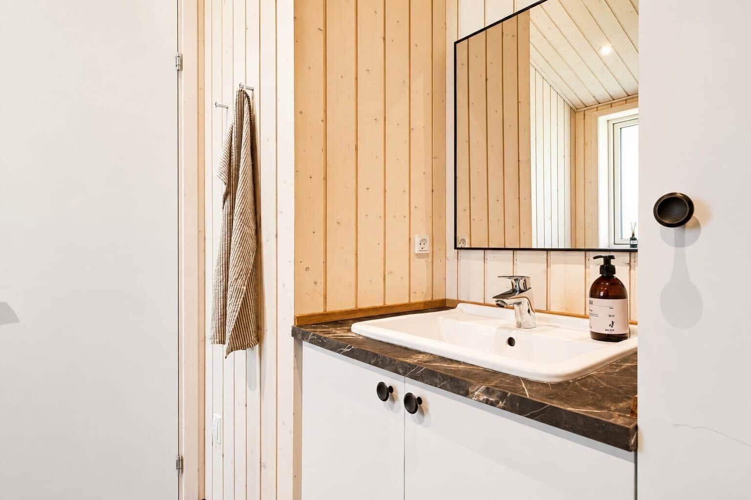 Waschbecken mit Spiegel, Holzwand und dunkler Arbeitsplatte.
