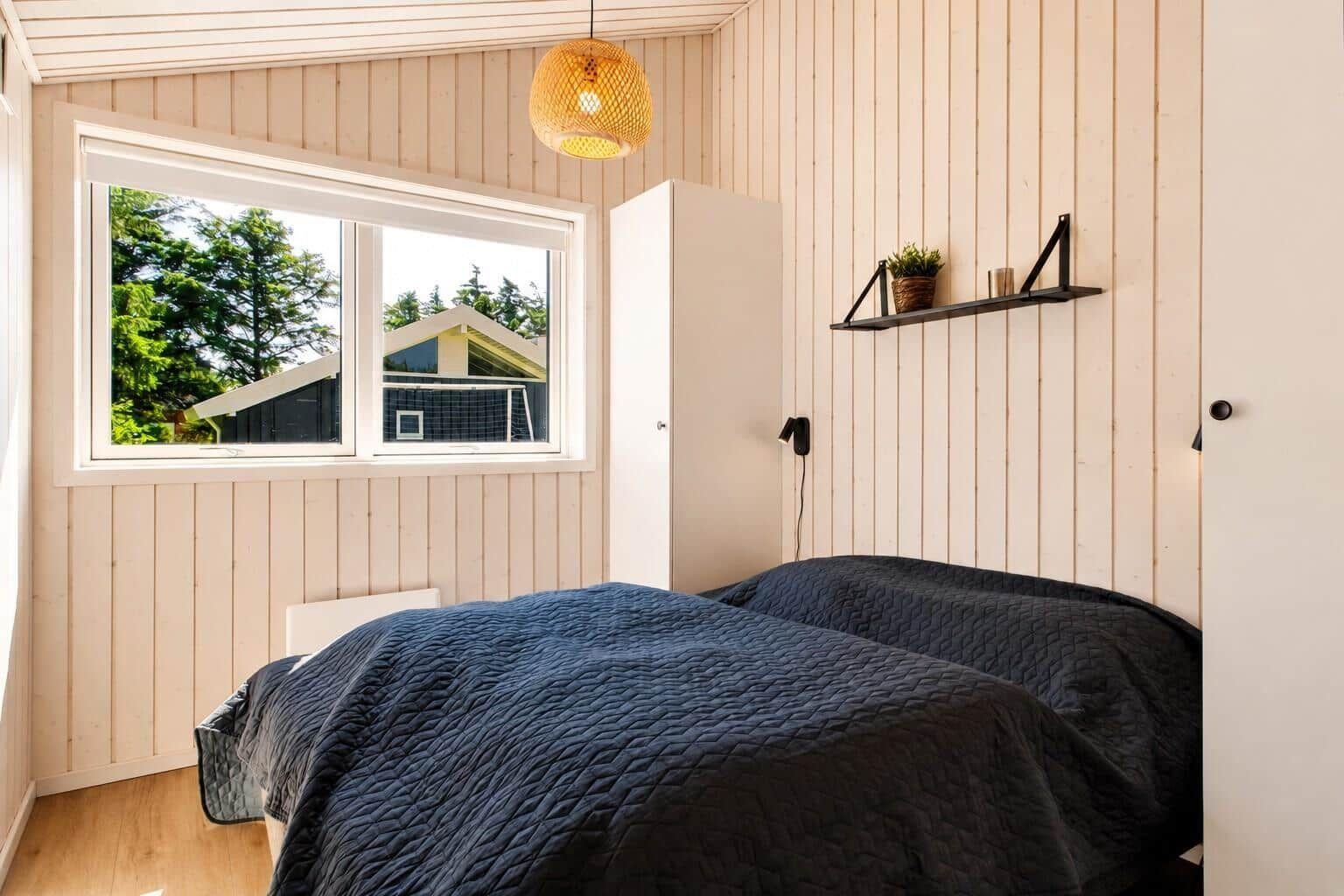 Schlafzimmer mit Bett, Fenster und Wandregal.