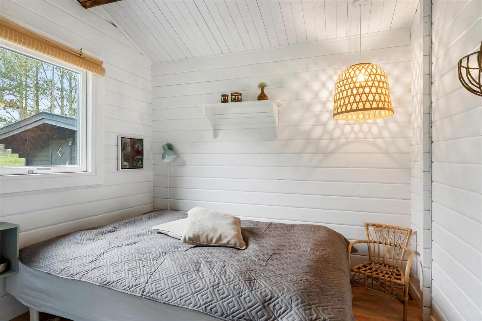 Schlafzimmer mit Bett, Wickerstuhl und Wandbild. Holzwand und Dachschräge.