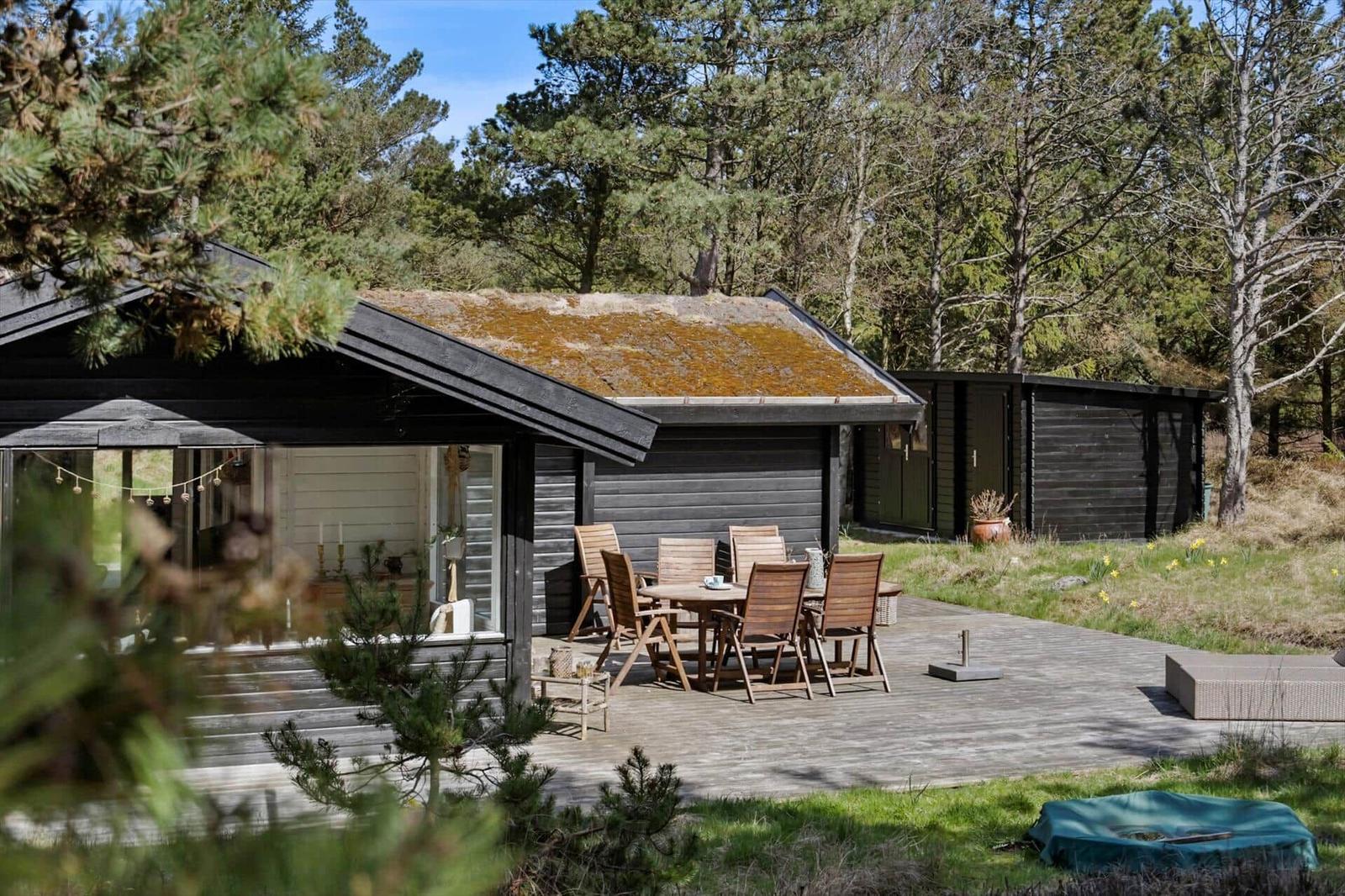 Haus mit grüner Dachdeckung und Holzfassade. Eingang mit Tisch und Blumen.