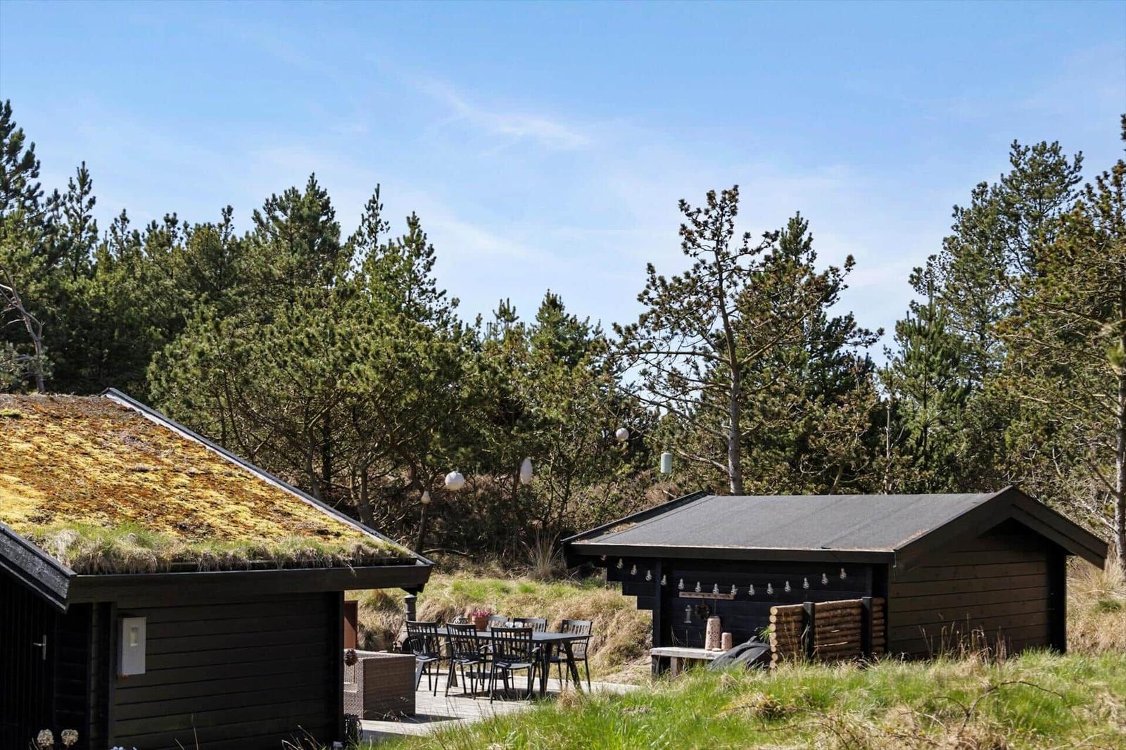 Ein Haus mit Grasdach, Terrasse und Garten. Möbel sind draußen platziert.