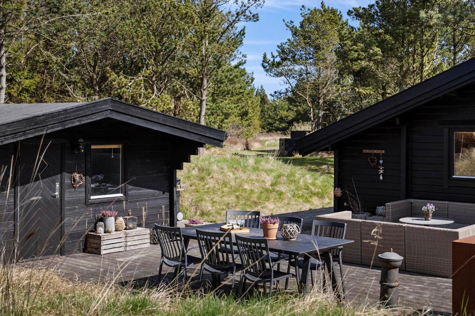 Holzhaus mit Terrasse und Garten. Im Inneren sind Möbel und Dekoration sichtbar.