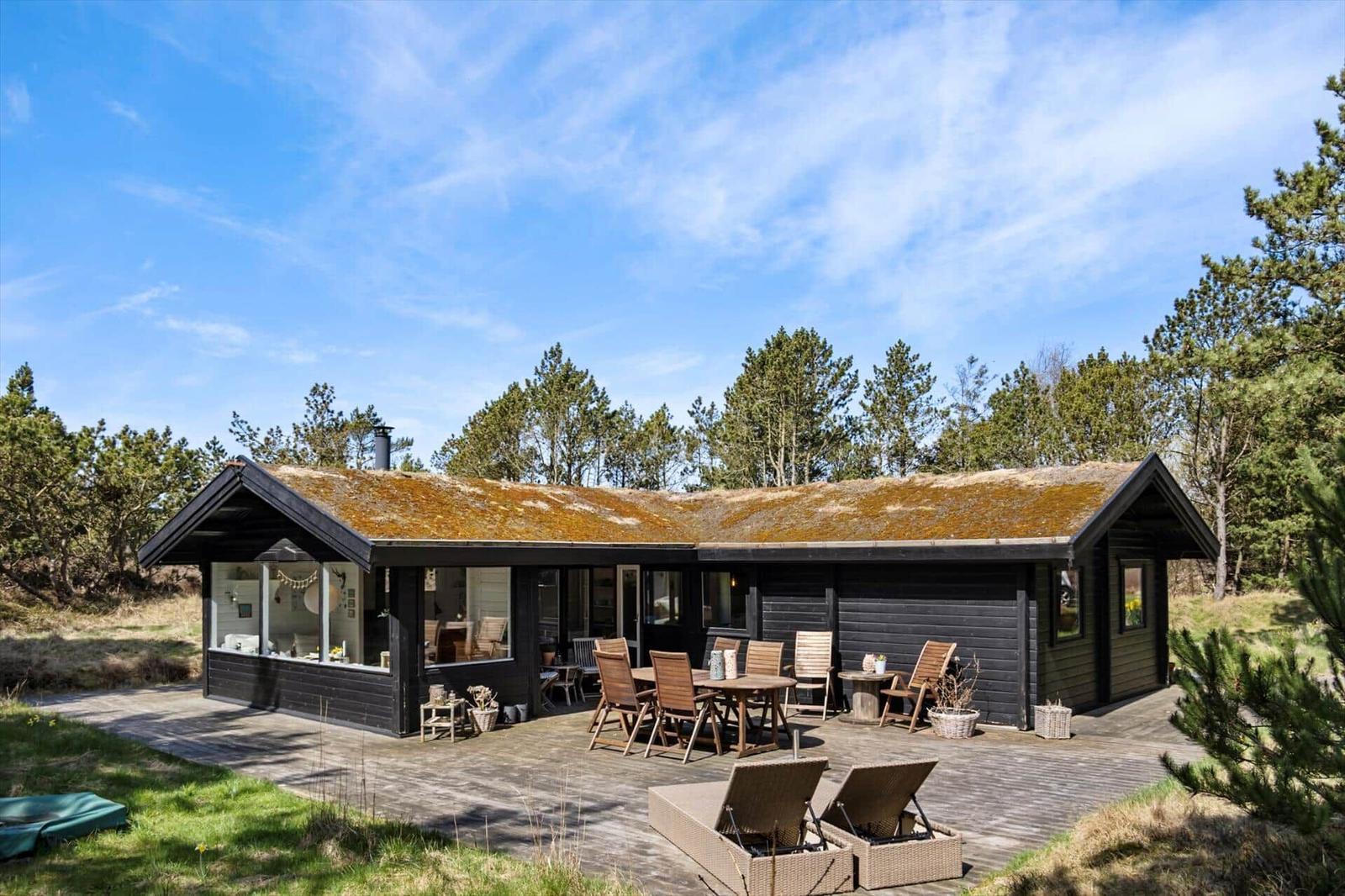 Holzhaus mit grüner Dachdeckung, umgeben von Bäumen und Gras