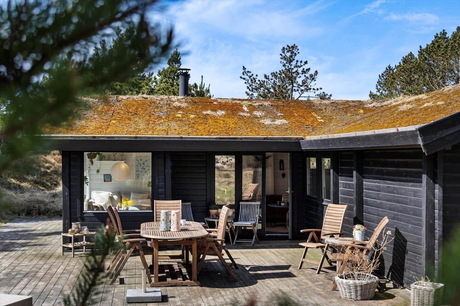 Wohnraum mit Kamin, Sofa und Blick auf Garten. Holzbalken an der Decke.